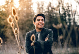 A man stood in a field next to some teasel plants with a wide smile, possibly benefiting from nighttime aligners.
