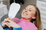 Woman in a dentist’s office holding a mirror and smiling, to symbolize the benefits of cosmetic dentistry.
