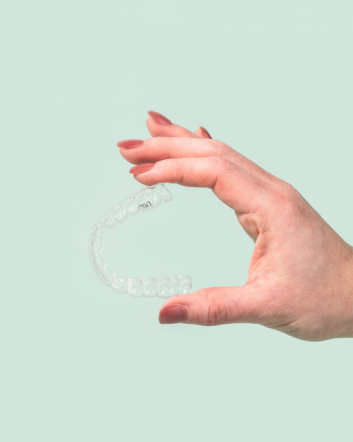 Hand holding a clear night guard against a mint green background