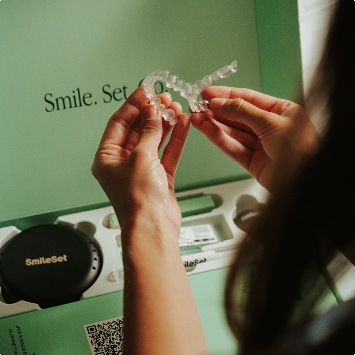 Clear aligners held over an open SmileSet kit