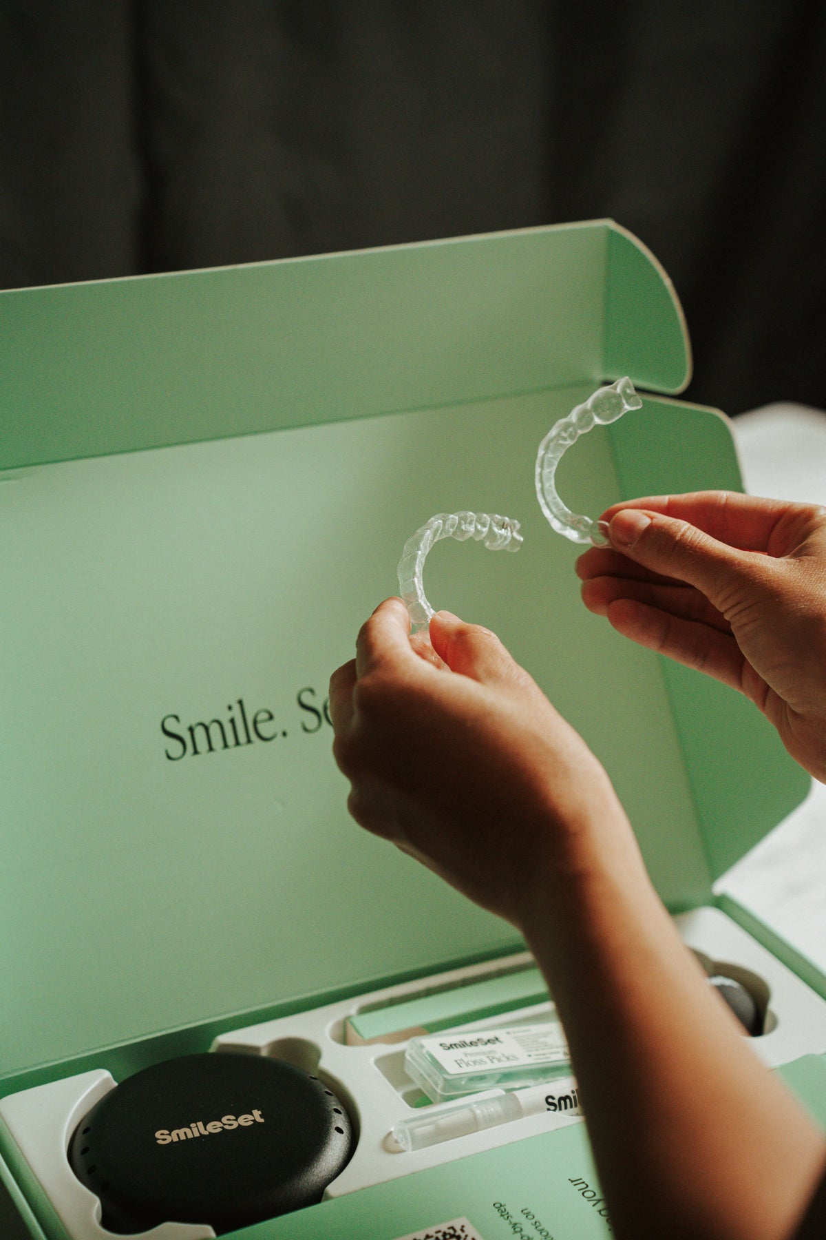 Hands holding two clear trays over a SmileSet box