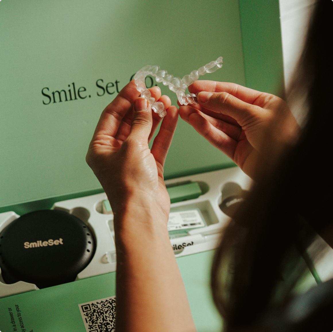 Hands holding a clear SmileSet aligner over its box