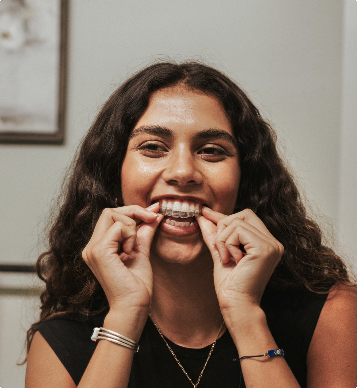 Woman smiling while placing a clear aligner on her teeth