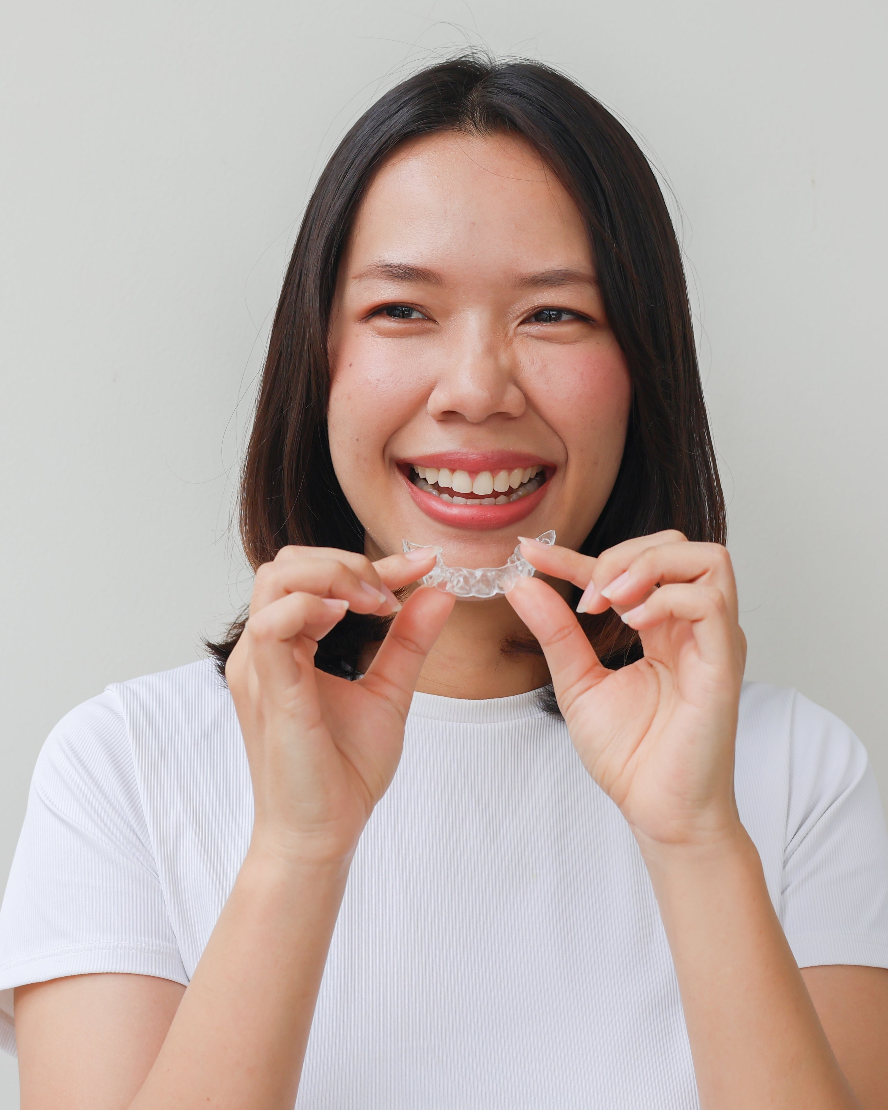 Woman holding a clear dental aligner against a plain background